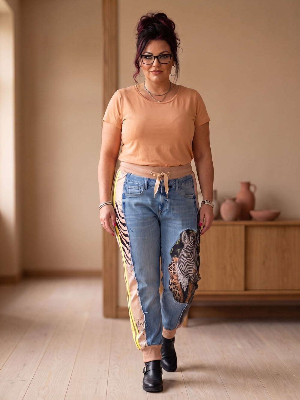 Jeans-Sweathose Wild & Unique mit Zebramotiv getragen – Curvy Model in Ganzkörperansicht, Zebra-, Leoparden- und Giraffendruck mit Strass am linken Bein, Zebrastreifen mit gelbem Streifen am rechten Bein, dazu schlichtes Apricot-Shirt und schwarze Boots, in großen Größen von CurvyRausch
