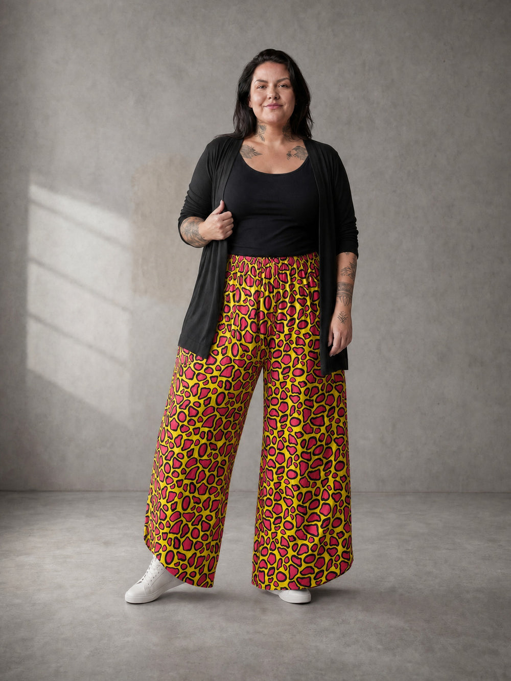 Curvy Model trägt die Pumphose Neon Leo Love in Lime mit pinkfarbenem Leo-Print zu schwarzem Top und langer schwarzer Strickjacke, dazu weiße Sneaker – in großen Größen von CurvyRausch